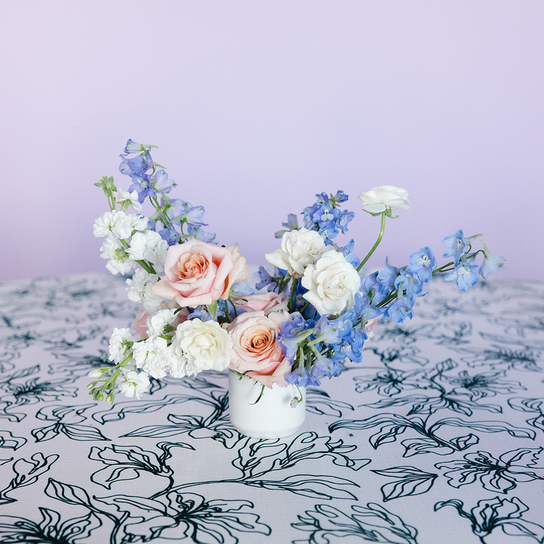 A floral centerpiece with orange and purple flowers in a white vase, placed on a table with orange and yellow striped tablecloth.