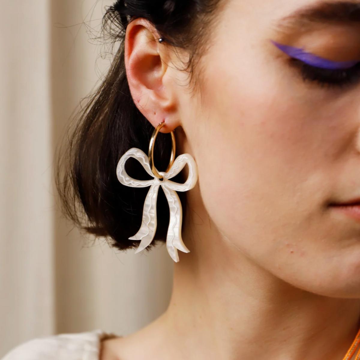 Close-up of a person wearing a bow-shaped earring with a blurred background