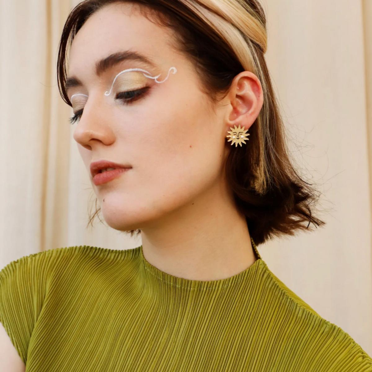 Woman wearing a gold earring with a beige background