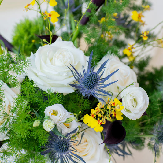 Floral arrangement with white roses, purple callas, and yellow flowers on a white background