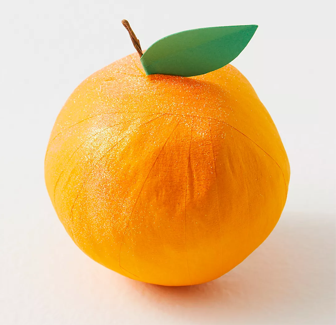 A crepe paper orange with a green leaf on top, designed as a surprise gift with layers of ribbon and a vintage-inspired keepsake inside.