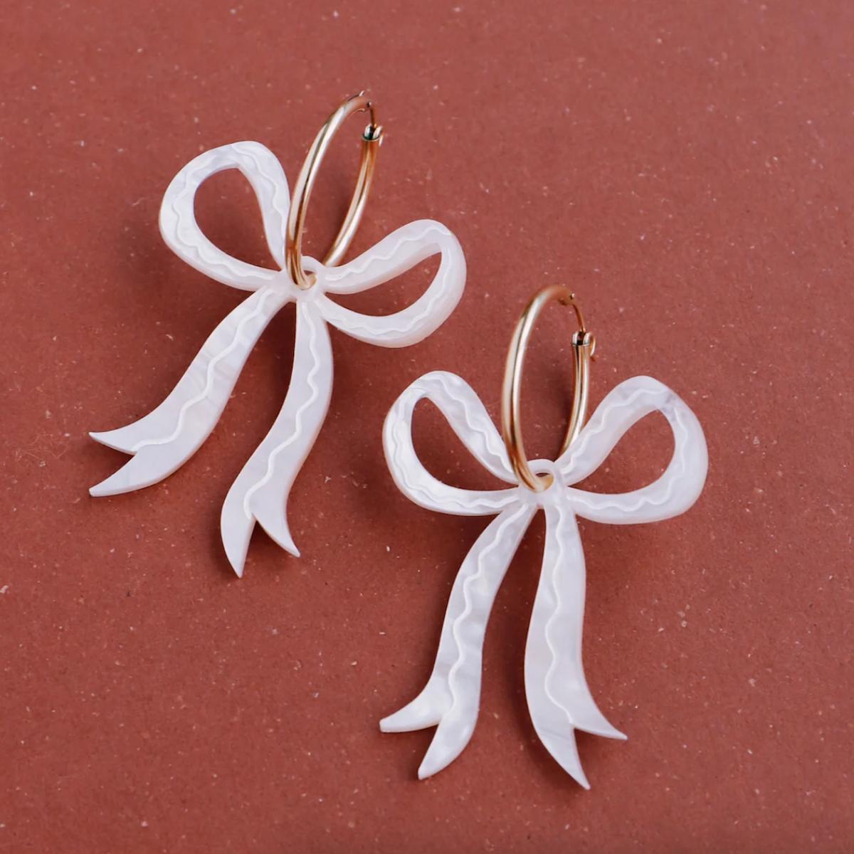 White bow-shaped earrings on a pink background