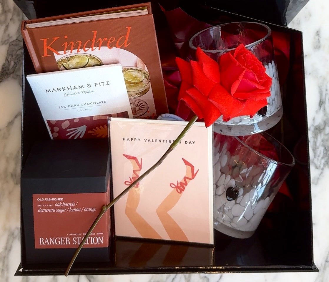 Valentine's Day gift box with a rose, chocolate, and other items on a marble surface