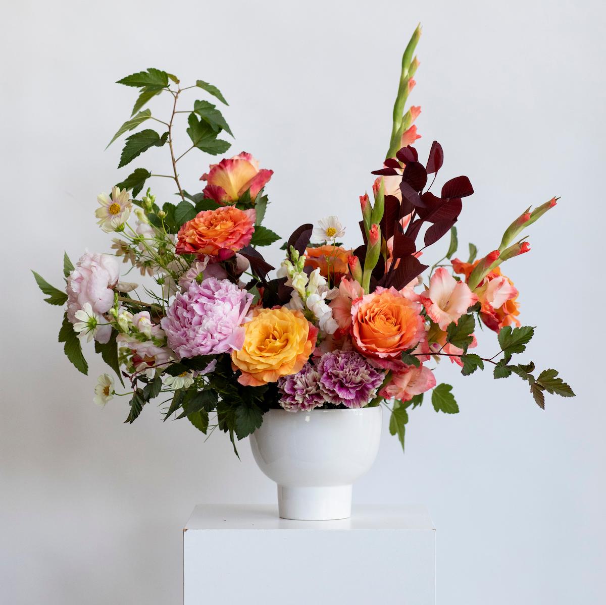 colorful floral centerpiece on a white background with a white circle vase