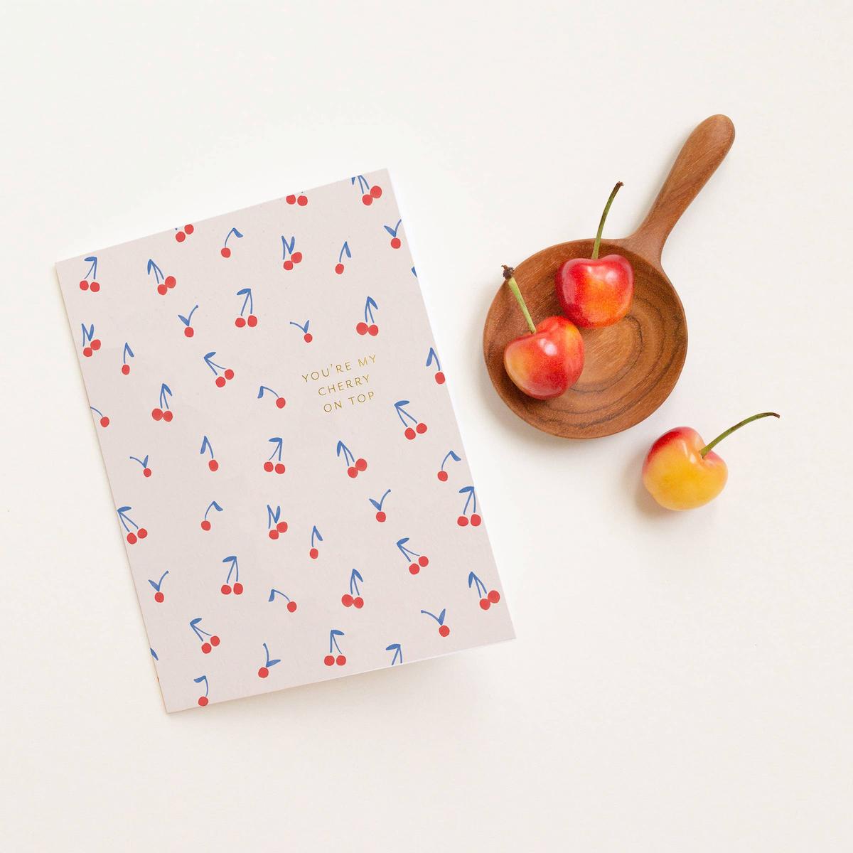 Notebook with cherry pattern on a white surface with cherries and a wooden plate.