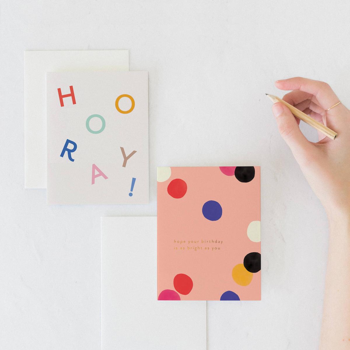 Three greeting cards on a white surface with a hand holding a pen.