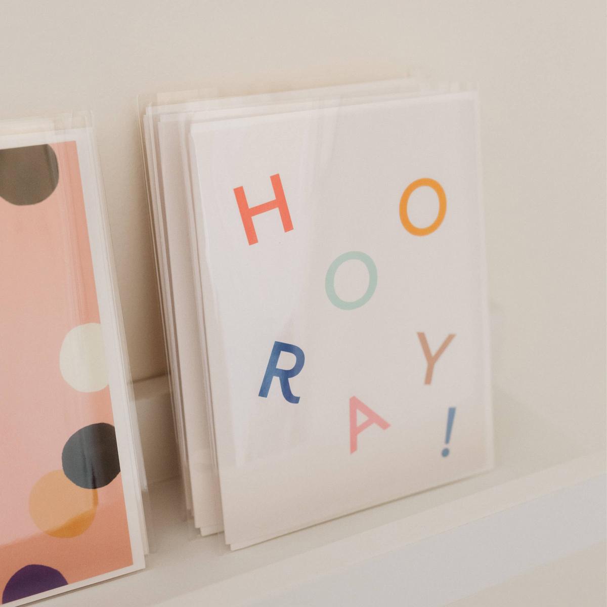 Stack of greeting cards with 'HOORAY!' text on a white surface