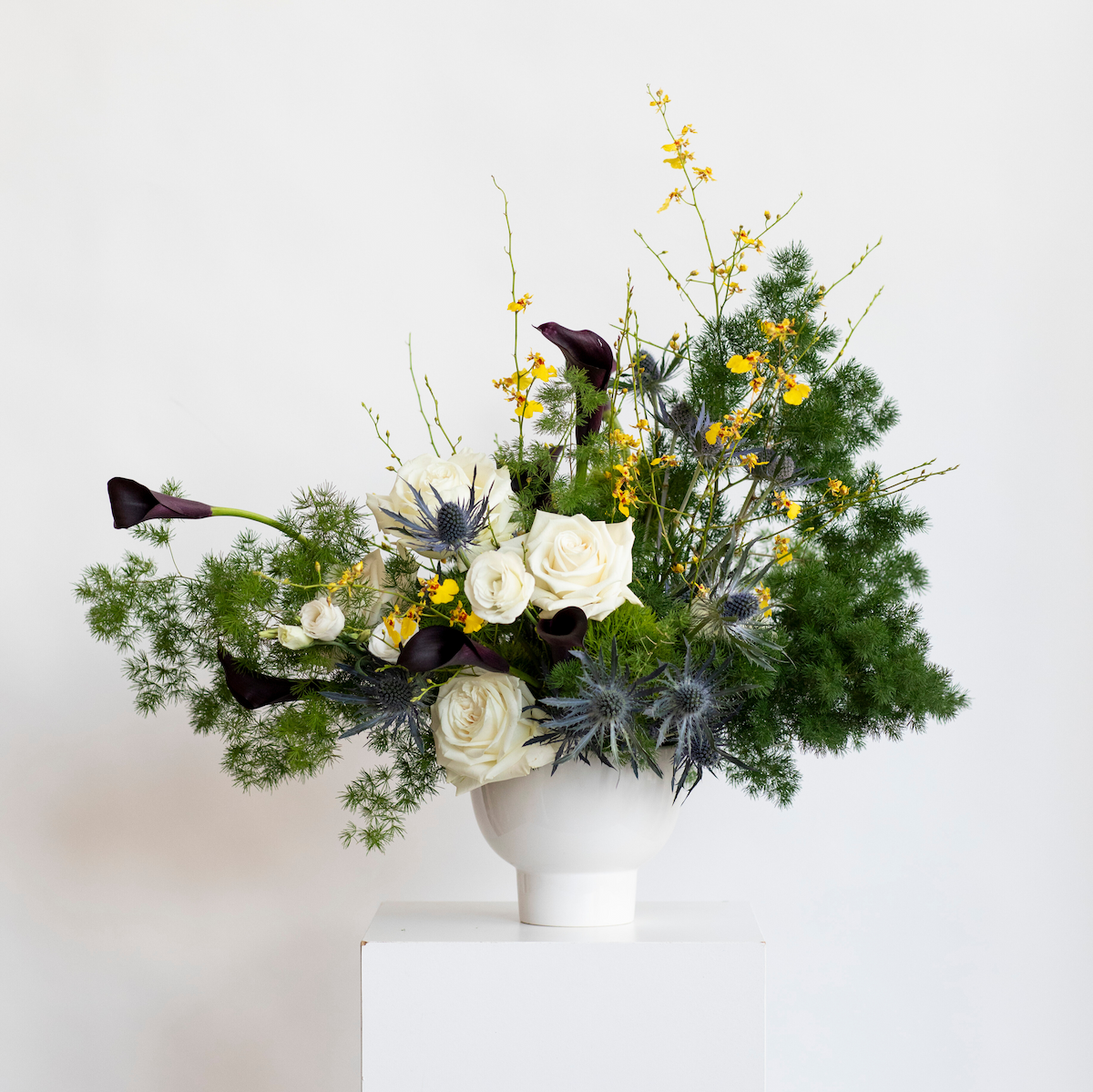 Floral arrangement with white roses, yellow flowers, and greenery in a white vase on a light background