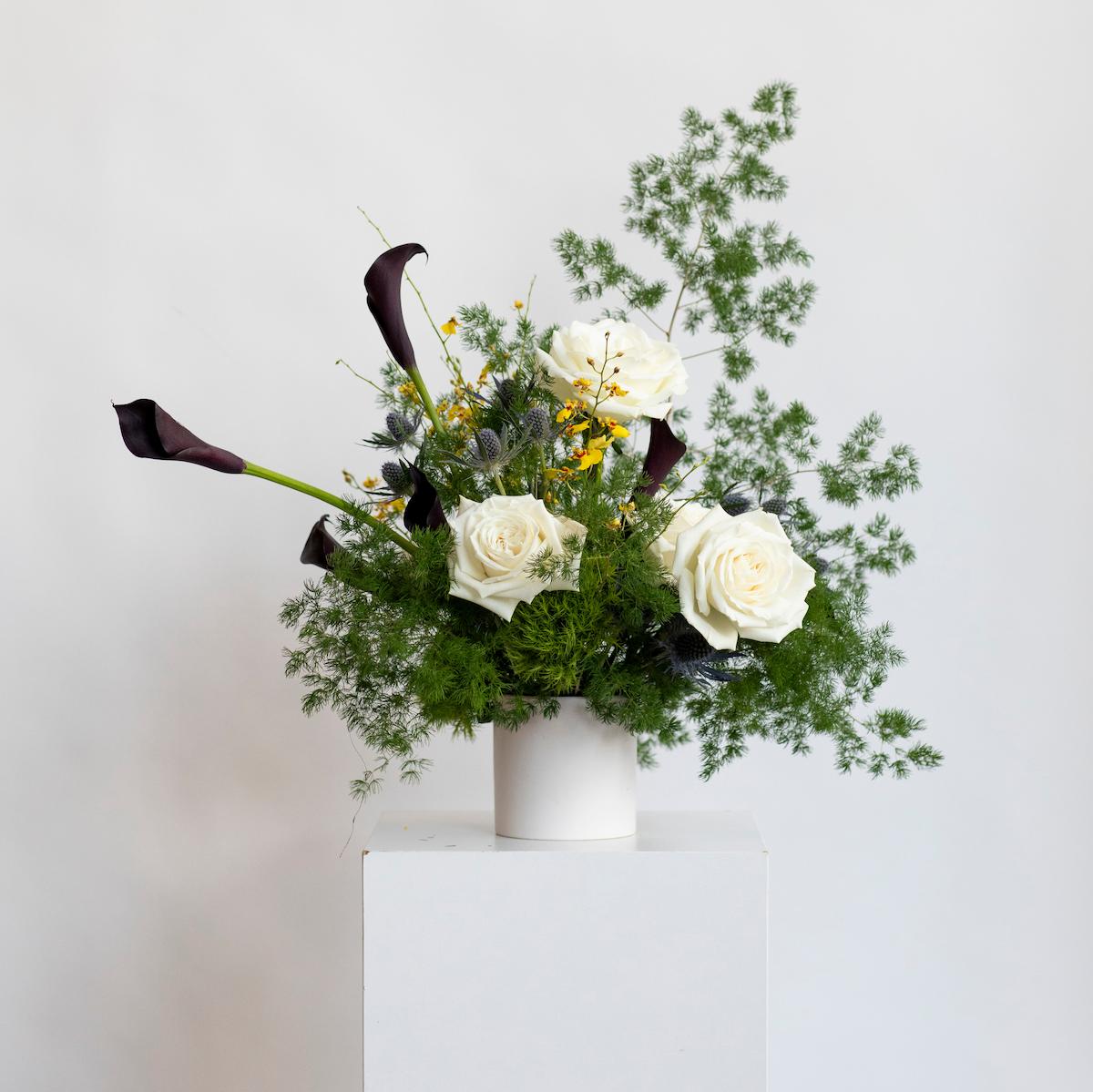 Floral arrangement with white roses, greenery, and a white vase on a light gray background