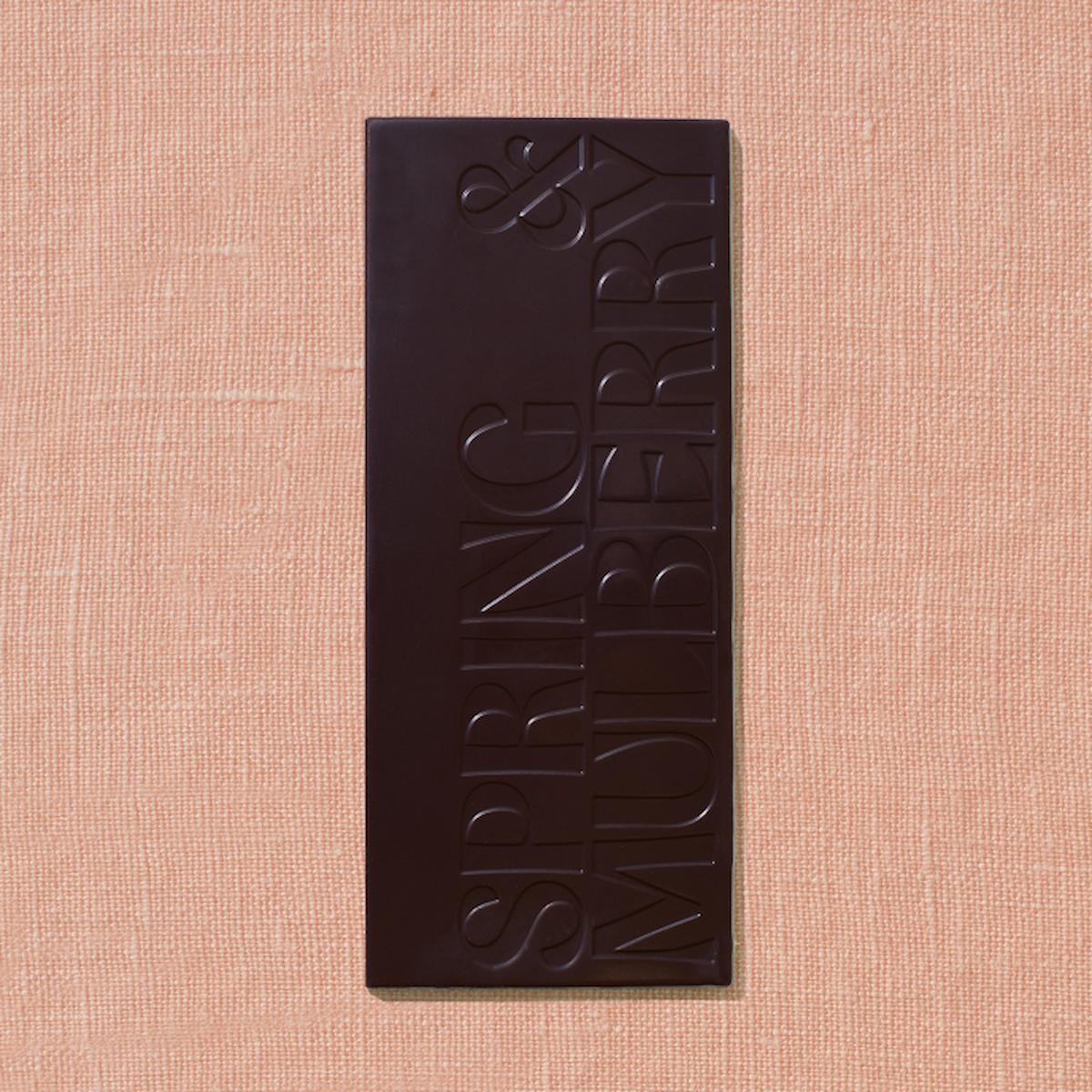 Dark chocolate bar with 'Spring & Mulberry' branding on a beige fabric background