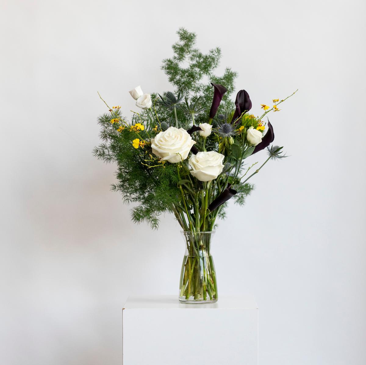 Bouquet of flowers in a clear vase on a white surface with a light gray background