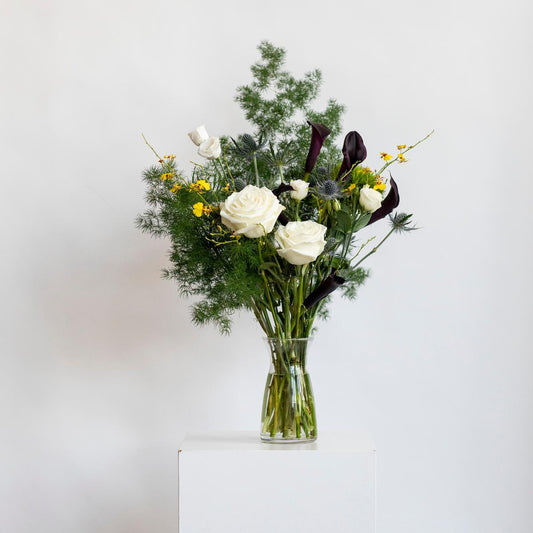 Bouquet of flowers in a clear vase on a white surface with a light gray background