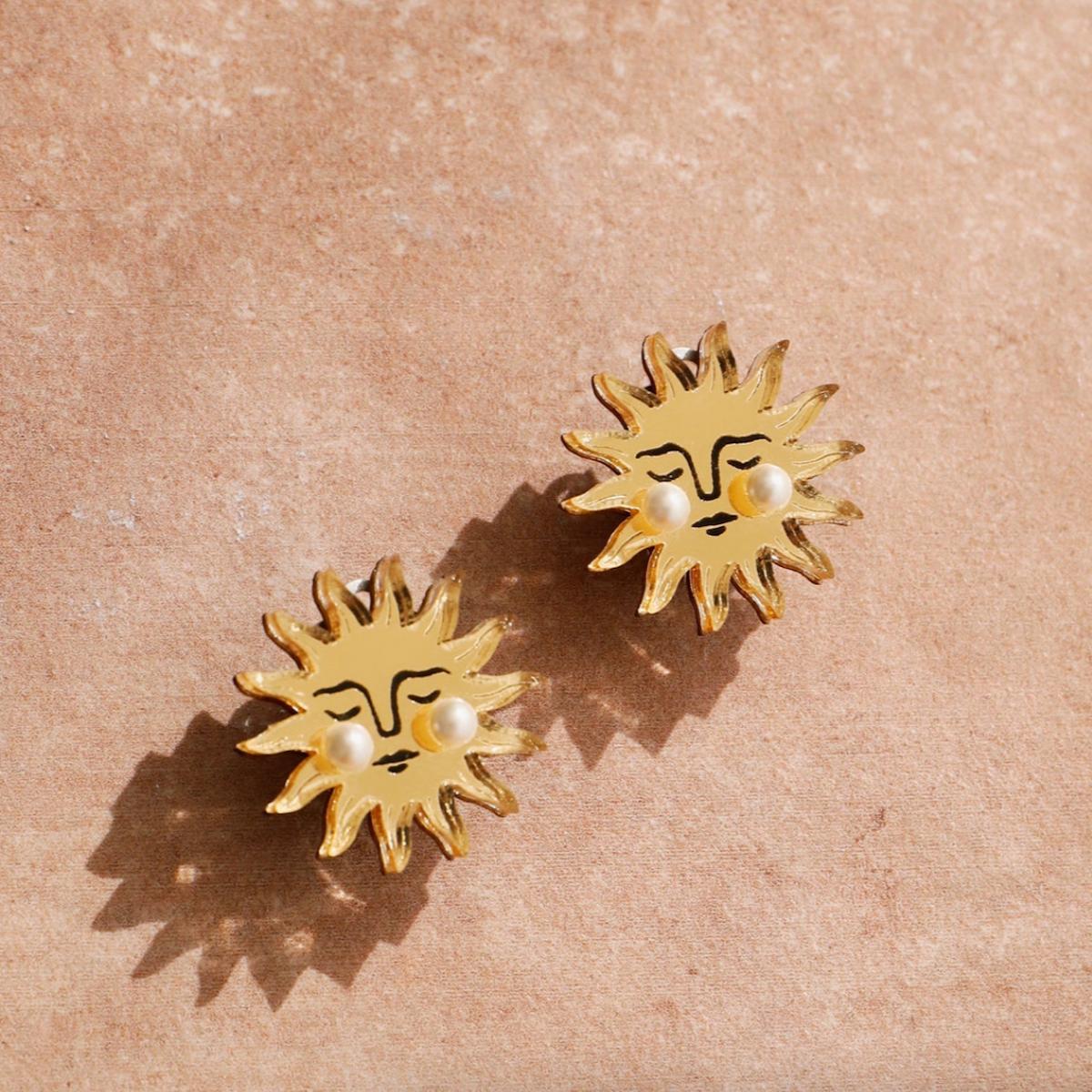 Gold sun-shaped earrings with pearl centers on a beige background